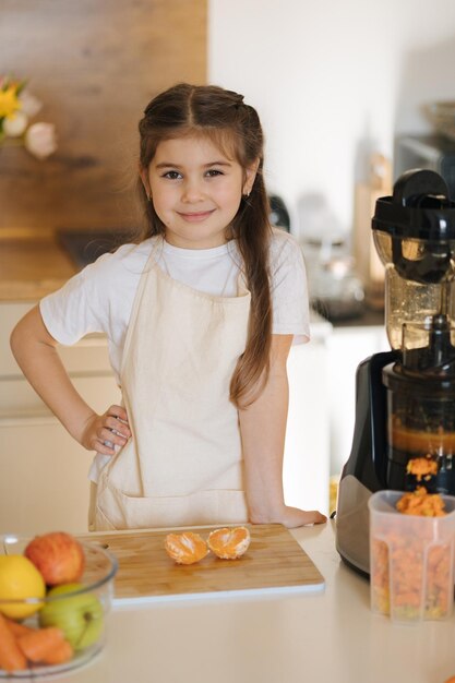 Adorable niña en delantal de pie en la mesa de la cocina llena de verduras y frutas orgánicas