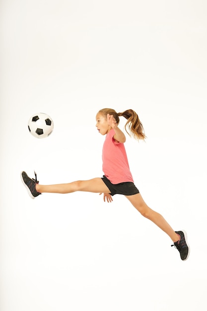 Adorable niña deportiva saltando y jugando al fútbol