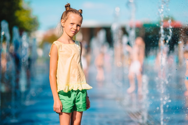 Adorable niña divertirse en la fuente de la calle en un día caluroso y soleado