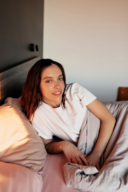 Adorable niña encantadora con cabello oscuro y ondulado se despierta por la mañana y se acuesta en la cama con una sonrisa feliz