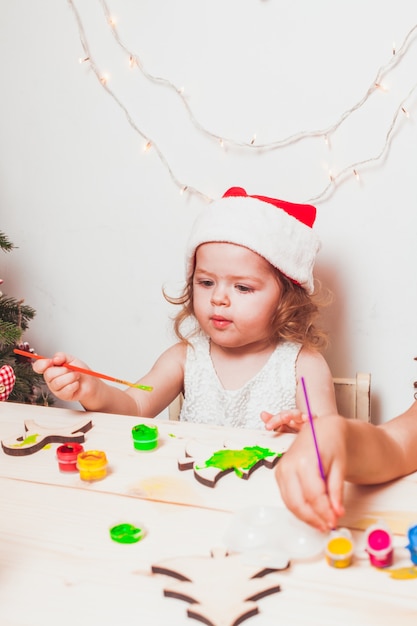 Adorable niña está pintando figuras navideñas de madera