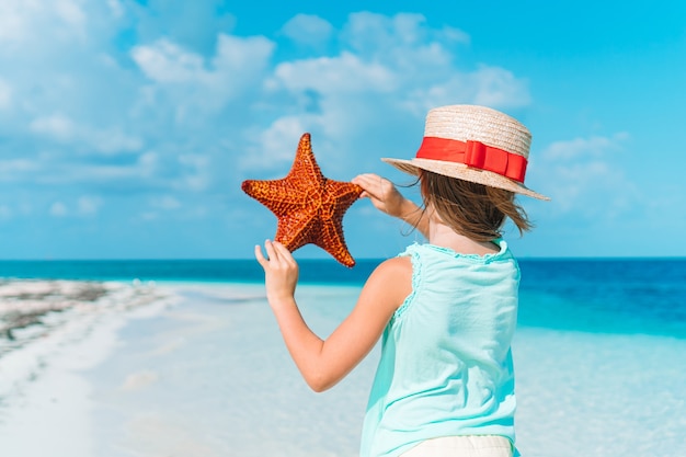 Adorable niña con estrellas de mar en la playa vacía blanca