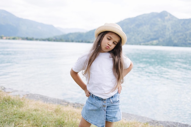 Adorable niña con falda de mezclilla, camiseta blanca y paja de panamá parada frente a una gran hermosa