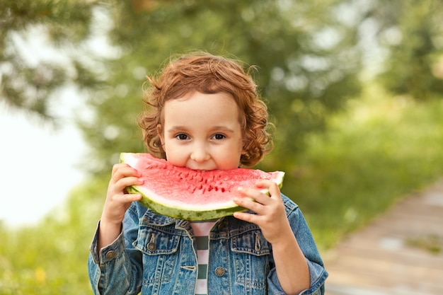 Adorable niña feliz come una rodaja de sandía madura al aire libre.