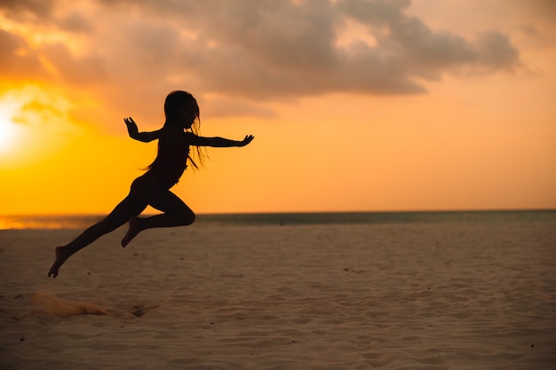 Adorable niña feliz en la playa blanca al atardecer.