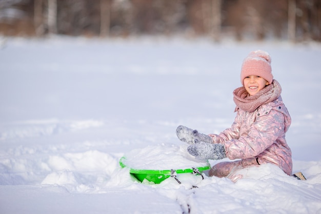 Adorable niña feliz en trineo en día de invierno cubierto de nieve.