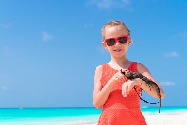 Adorable niña felizmente sostiene un lagarto tropical salvaje en la playa tropical blanca