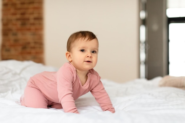 Adorable niña gateando en la cama y mirando a la cámara en el espacio libre interior del dormitorio