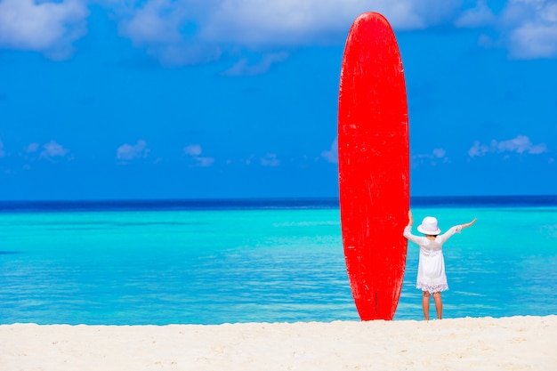 Adorable niña con gran tabla de surf durante vacaciones tropicales