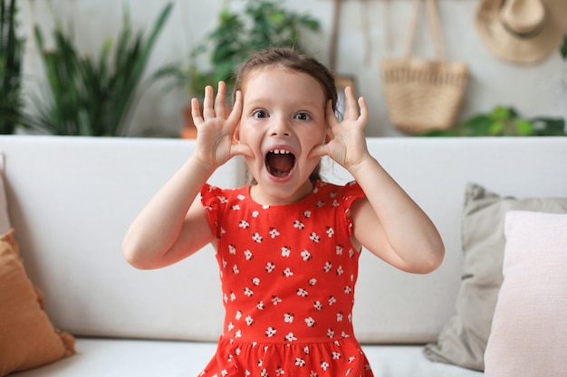 Adorable niña haciendo muecas mientras está sentado en el sofá de la sala de estar.