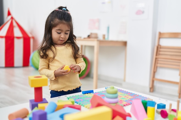 Adorable niña hispana jugando con bloques de construcción de pie en el jardín de infantes