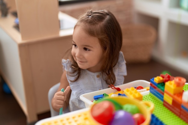 Adorable niña hispana jugando con bloques de construcción sentados en la mesa en el jardín de infantes