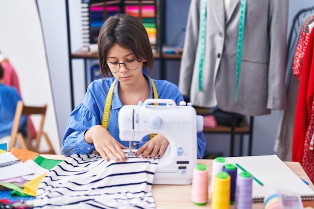 Adorable niña hispana sastre usando máquina de coser en fábrica de ropa