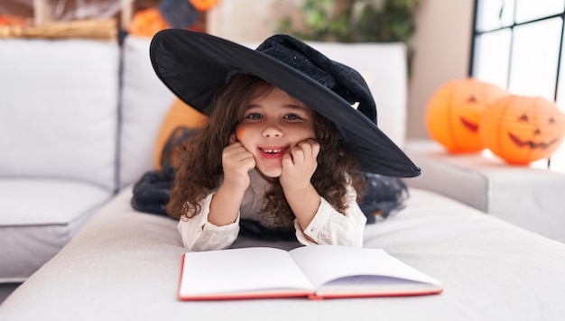 Adorable niña hispana con traje de halloween leyendo un libro en casa