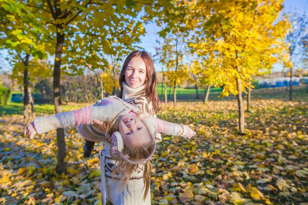 Adorable niña y joven madre divirtiéndose en el parque otoño en día soleado