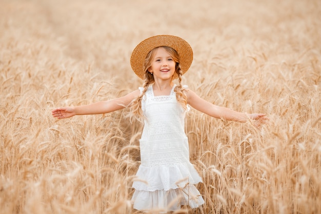 Adorable niña juega en un campo de trigo en un cálido día de verano