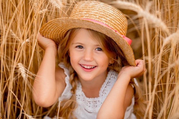 Adorable niña juega en un campo de trigo en un cálido día de verano