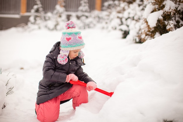 Adorable niña juega con nieve palear en un día de invierno