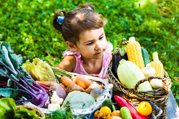 Adorable niña juega con una variedad de verduras en el césped