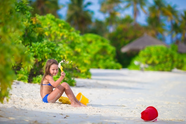 Adorable niña jugando con juguetes de playa durante vacaciones tropicales