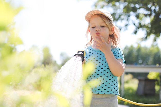 Adorable niña jugando con una manguera de jardín en un caluroso y soleado día de verano