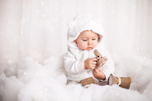 Adorable niña jugando con un oso de peluche en un algodón como nieve artificial