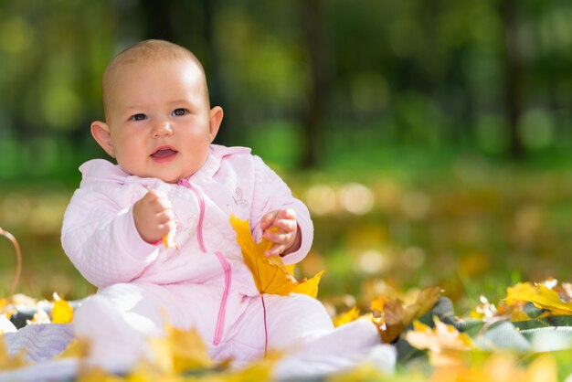 Adorable niña jugando en un parque de otoño sentado en el suelo entre coloridas hojas amarillas con espacio de copia