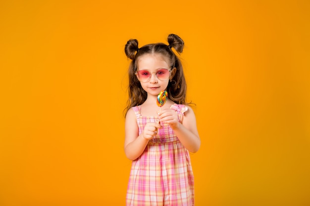 Adorable niña lamiendo paleta, en espacio amarillo