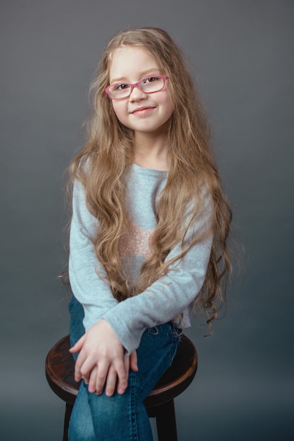 Adorable niña linda con el pelo largo y rubio con gafas y ropa casual en estudio fotográfico