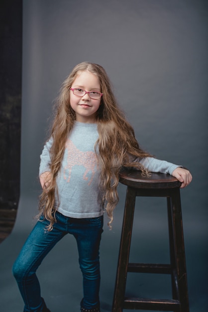 Adorable niña linda con el pelo largo y rubio con gafas y ropa casual en estudio fotográfico