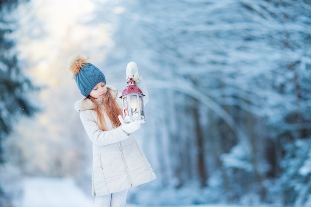 Adorable niña con linterna en Navidad en el bosque de invierno al aire libre