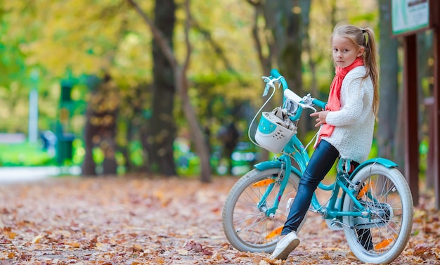 Adorable niña montando una bicicleta en el hermoso día de otoño al aire libre