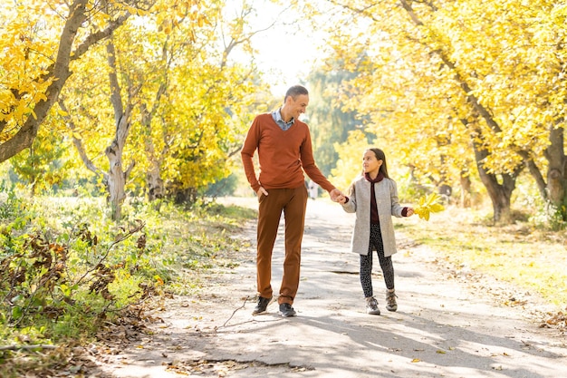 Adorable niña con padre feliz caminando en el parque de otoño en un día soleado.