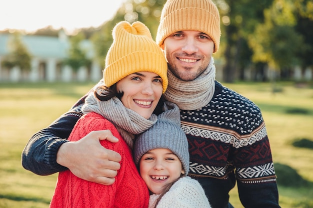 Adorable niña parada cerca de sus afectuosos padres disfrutan pasar tiempo juntos abrazarse sonreír felizmente mirar directamente a la cámara Momentos agradables e inolvidables con la familia