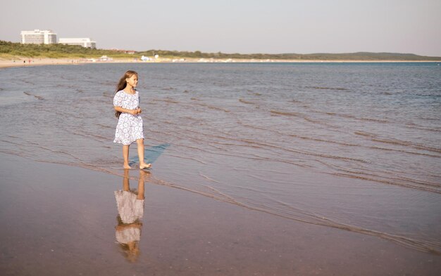 Adorable niña con el pelo largo al aire libre caminando y disfrutando de la puesta de sol en la playa en un día de verano