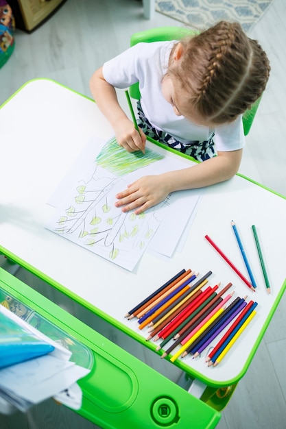 Adorable niña pequeña dibujando con lápices en casa sentado en la mesa. Niño creativo sentado en una habitación aprendiendo a dibujar. Niña pequeña haciendo los deberes en casa.