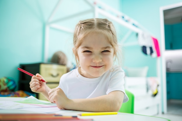 Adorable niña pequeña dibujando con lápices en casa sentado en la mesa. Niño creativo sentado en una habitación aprendiendo a dibujar. Niña pequeña haciendo los deberes en casa.