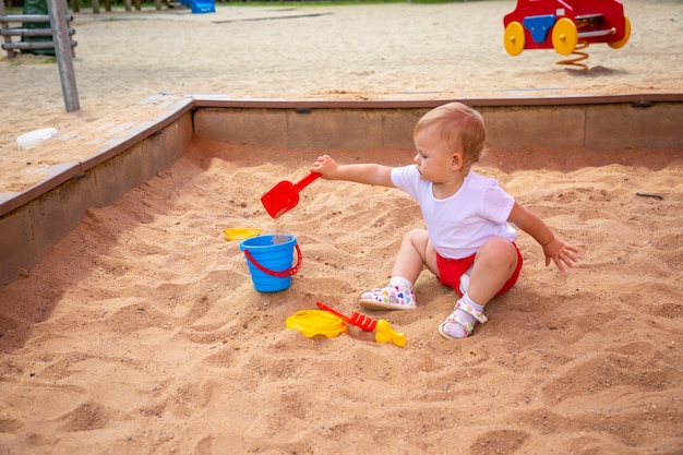 Adorable niña pequeña jugando con arena en el arenero en el patio de recreo