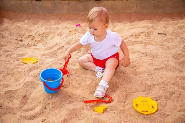 Adorable niña pequeña jugando con arena en el arenero en el patio de recreo