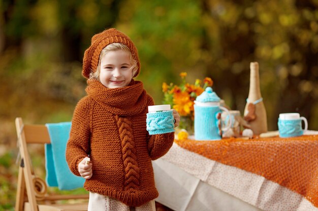 Adorable niña de picnic en el parque de otoño. Niña linda con una fiesta de té al aire libre en el jardín de otoño. Chica bebiendo té. Años de infancia felices. Concepto estacional.