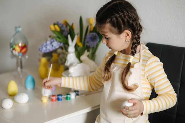 Adorable niña pintando huevos en la cocina en casa linda chica en delantal fondo de pascua