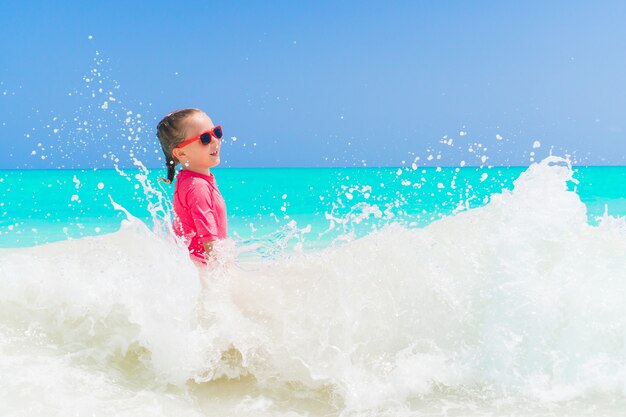 Adorable niña en la playa divirtiéndose mucho en el agua