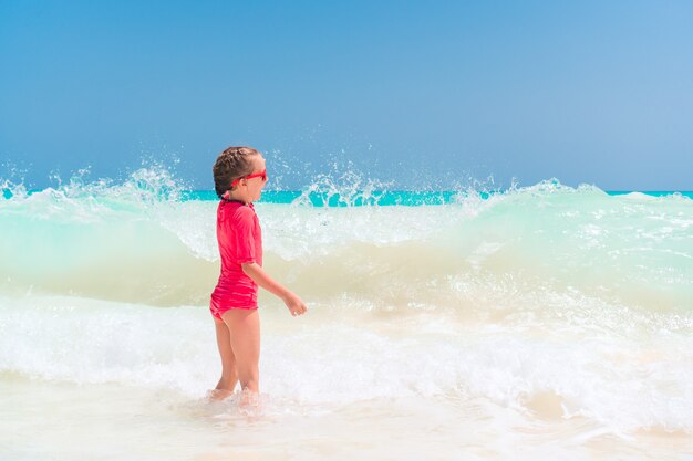 Adorable niña en la playa divirtiéndose mucho en el agua