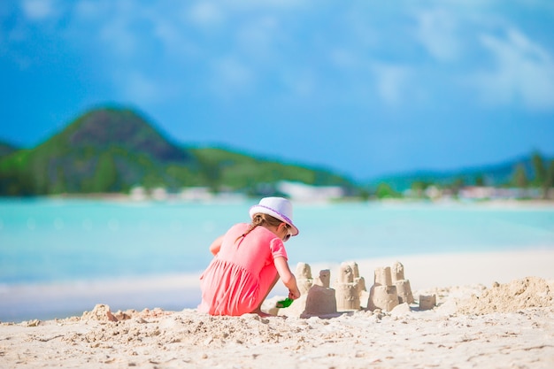 Adorable niña en la playa tropical haciendo castillos de arena