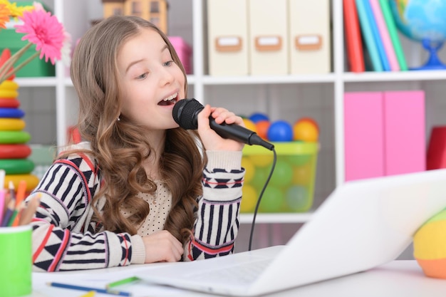 Adorable niña con portátil moderno y cantando karaoke