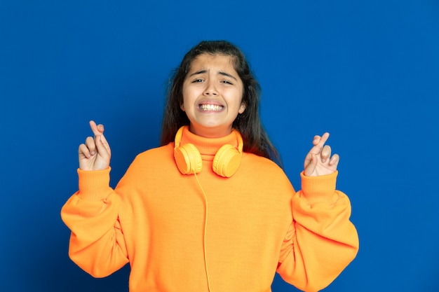 Foto adorable niña preadolescente con jersey amarillo gesticulando sobre la pared azul