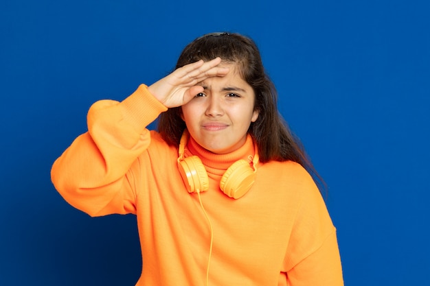 Foto adorable niña preadolescente con jersey amarillo gesticulando sobre la pared azul