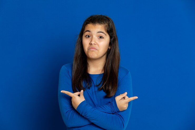 Foto adorable niña preadolescente con jersey azul gesticulando sobre la pared azul