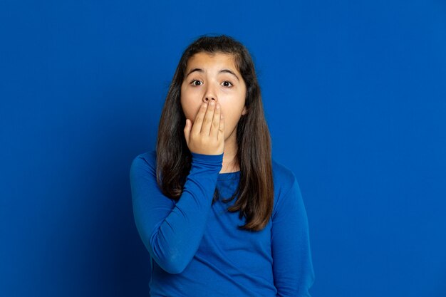 Adorable niña preadolescente con jersey azul gesticulando sobre la pared azul