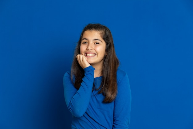 Foto adorable niña preadolescente con jersey azul gesticulando sobre la pared azul